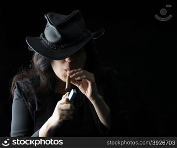 Young girl with a cigar in her mouth wearing black leather jacket and hat and holding a lighter up to the cigar