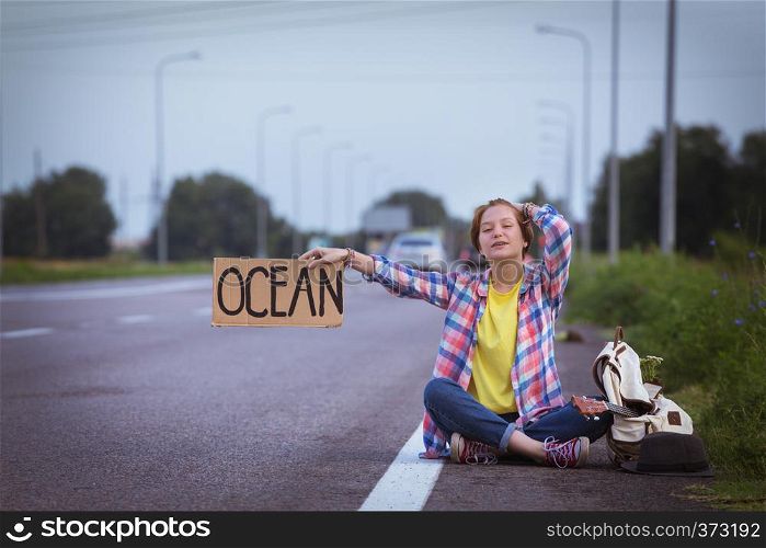 Young girl with a guitar coming along the road and hitch-hiking