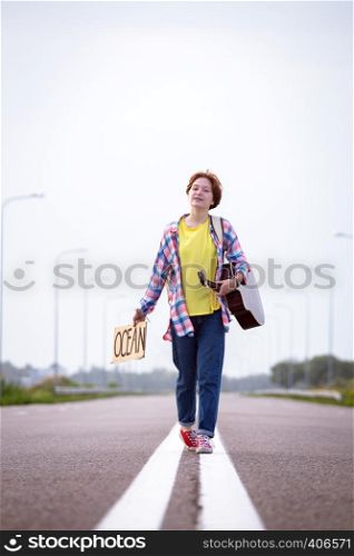 Young girl with a guitar coming along the road and hitch-hiking