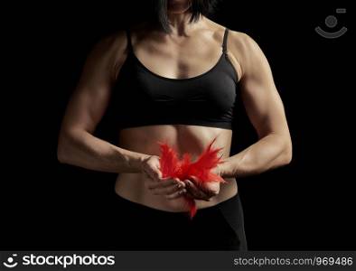 young girl with a muscular, athletic body is dressed in a black top and leggings, holding a bunch of red feathers. The muscles in the arms are tense, concept of strength and lightness, low key