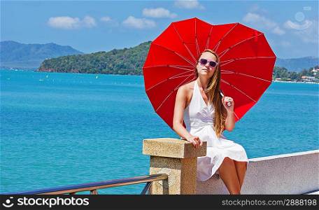 young girl with a red umbrella sits on the waterfront
