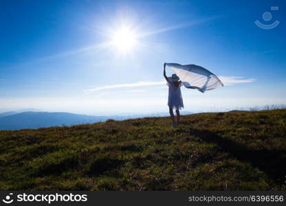 Young girl with a tissue raised up, enjoying sunlight at the top of the mountain. Unity of the girl with nature