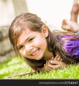 Young girl with big smile showing of her teeth, lying on the lawn of the back garden on a nice summer day.