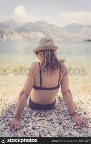 Young girl with bikini is sitting on the pebble beach. Italy.