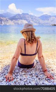 Young girl with bikini is sitting on the pebble beach. Italy.