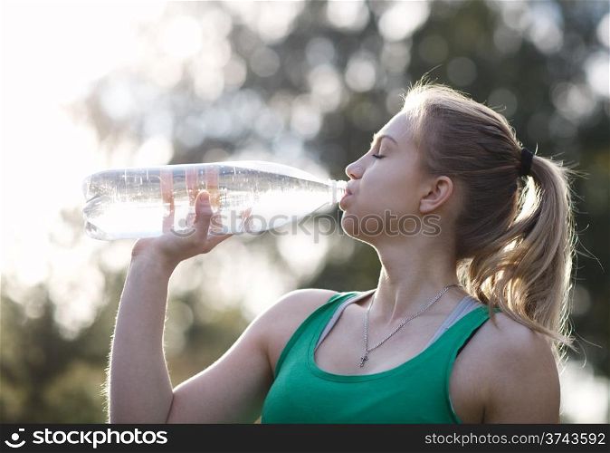 Young girl with closed eyes drinking water against a plants background