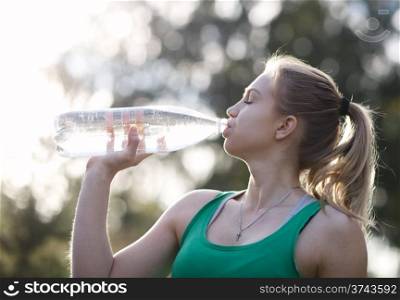 Young girl with closed eyes drinking water against a plants background