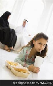 Young girl with fast food in living room with parents in background (high key/selective focus)
