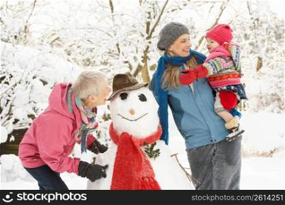Young Girl With Grandmother And Mother Building Snowman In Garden