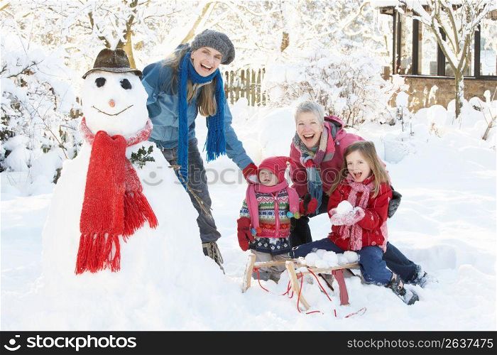 Young Girl With Grandmother And Mother Building Snowman In Garden