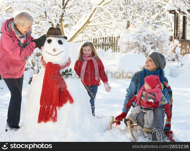 Young Girl With Grandmother And Mother Building Snowman In Garden