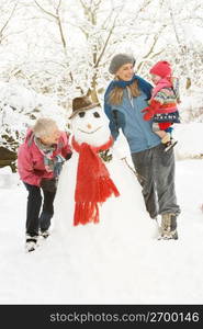 Young Girl With Grandmother And Mother Building Snowman In Garden