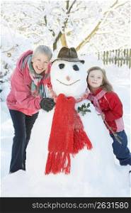 Young Girl With Grandmother Building Snowman In Garden