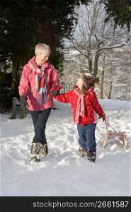 Young Girl With Grandmother Pulling Sledge Through Snowy Landscape