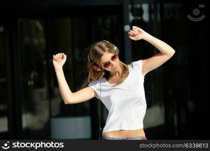 Young girl with headphones and sunglasses dancing in the street