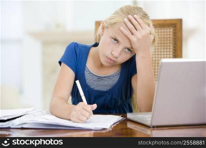 Young girl with laptop doing homework in dining room looking unhappy