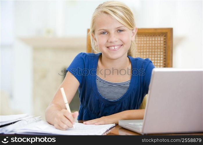 Young girl with laptop doing homework in dining room smiling