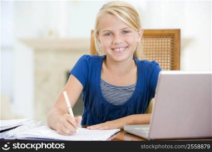 Young girl with laptop doing homework in dining room smiling