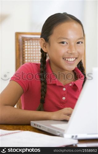 Young girl with laptop in dining room smiling