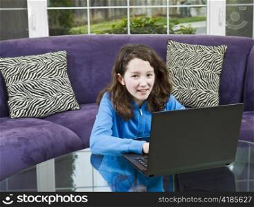 Young girl with laptop on glass table while sitting in front of couch