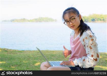 Young girl with laptop on the grass by the lake in park