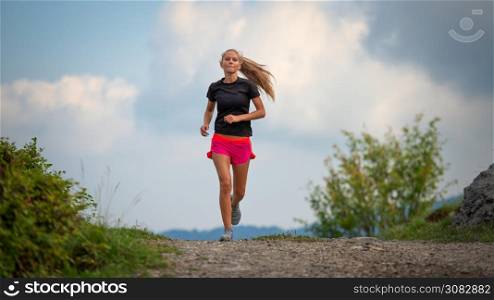 Young girl with lean physique running on hill dirt