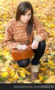 young girl with leather handbag sitting on yellow autumn leaf background