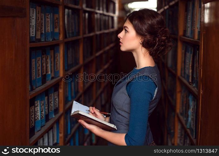 Young girl with notebook select textbook in college library.