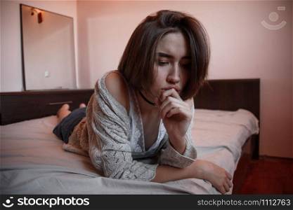 young girl with short hair in a sweater, denim skirt lying alone on the bed in the bedroom