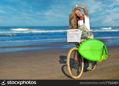 Young girl with surfboard and bicycle on the beach.