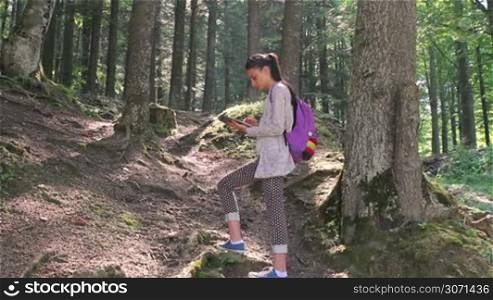Young girl with tablet computer hiking in the forest using travel app or map during her hike.