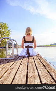 Young girl with white dress is sitting on a footbridge and enjoys the view over the lake.