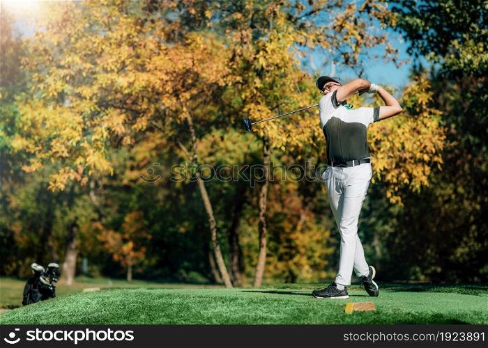 Young golfer on the tee box, hitting the ball with the driver club on a sunny autumn day