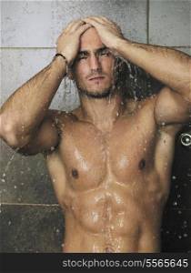 young good looking and attractive man with muscular body wet taking showe in bath with black tiles in background