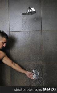 young good looking and attractive man with muscular body wet taking showe in bath with black tiles in background