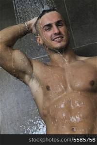 young good looking and attractive man with muscular body wet taking showr in bath with black tiles in background