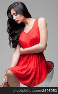 young gorgeous caucasian brunette in red dress on the chair, studio shot