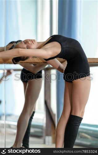 Young graceful ballet dancer stretching out at the barre in the studio