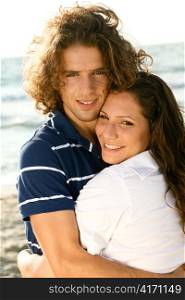 Young guy and lady smiling at camera while hugging on the beach