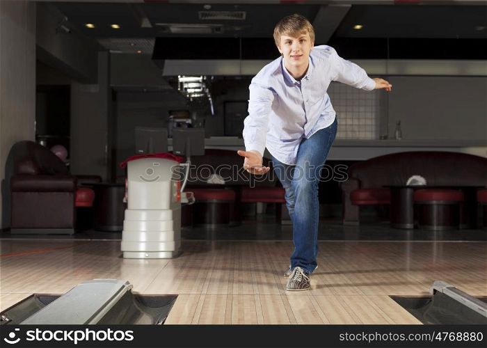 Young guy at bowling club throwing ball. Guy playing bowling
