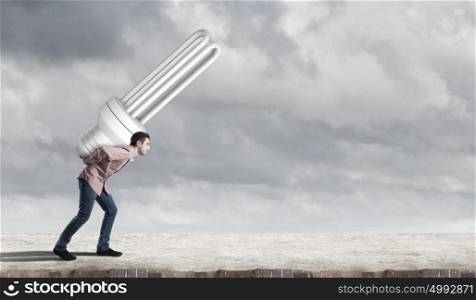 Young guy carrying light bulb on his back. Guy carrying light bulb