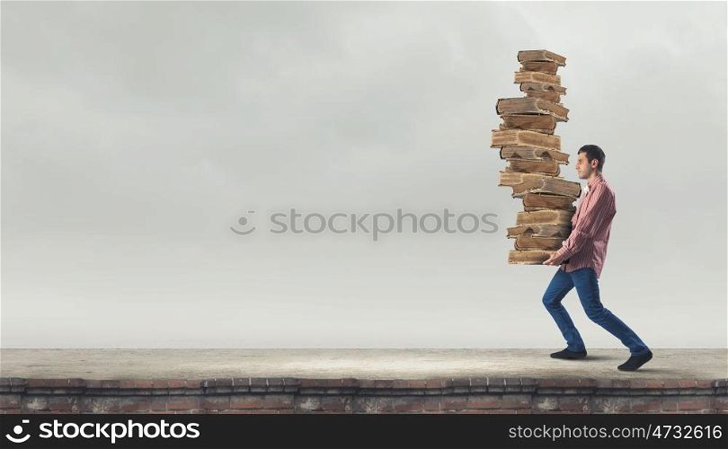 Young guy carrying pile of old books. I have to study hard