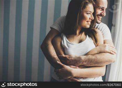Young guy embracing his girlfriend and both looking through window