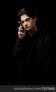 young guy in a black hoodie on a black background with a mobile phone in his hands