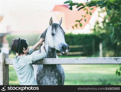 Young guy scratches his horse at summer outdoor nature
