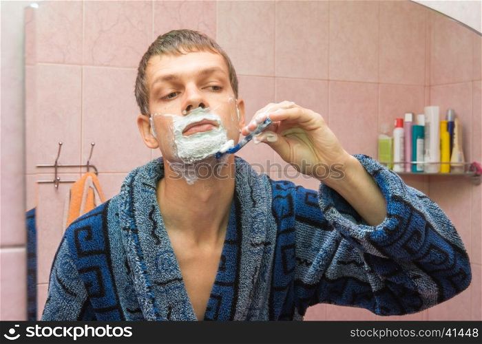 Young guy shaves neck in front of the mirror
