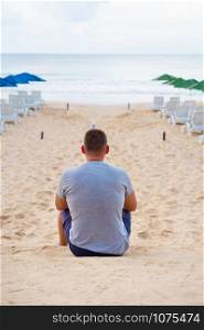Young guy sits with his back on a sandy beach.. Young guy sits with his back on a sandy beach
