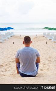 Young guy sits with his back on a sandy beach.. Young guy sits with his back on a sandy beach