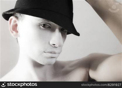 young guy with white makeup and black hat on light background