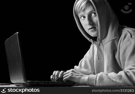 young hacker is sitting in hoody with laptop